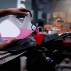 Mano versa liquido di raffreddamento rosa in un imbuto rosso, pronto a controllare il livello nel motore dell'auto.