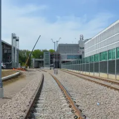 Budowa stacji Kraków-Balice PKP. Torowisko w budowie, nowoczesne budynki, dźwig.