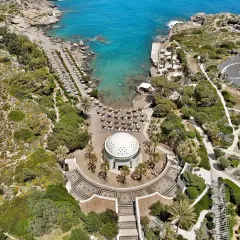 Vacker vy över Kallithea Beach med turkost vatten, solstolar och en kupolformad byggnad.