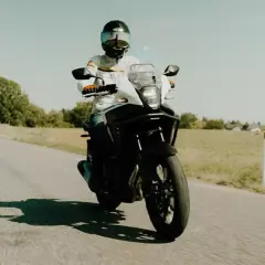Motocyklista w kasku jedzie motocyklem turystycznym po wiejskiej drodze. Idealny na kategorię A2.