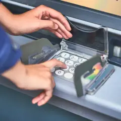 Dłoń wprowadza PIN do bankomatu, pokazując, jak włożyć kartę do bankomatu i dokonać transakcji.