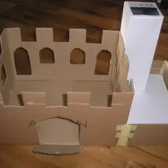 Zbudowana z kartonu makieta zamku z blankami i łukowymi oknami, z wysoką wieżą.