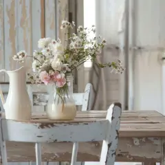 Un tavolo di legno consumato, sedie bianche sbiadite e un vaso di fiori bianchi e rosa creano un'atmosfera romantica con un **effetto shabby**.