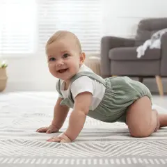 Uśmiechnięte 8 miesięczne dziecko na czworakach na dywanie.