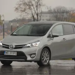 Srebrny minivan Toyota Verso zaparkowany na mokrej nawierzchni w deszczowy dzień.