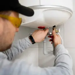 Fachowiec w okularach ochronnych dokonuje montażu bojlera elektrycznego, podłączając instalację wodną.