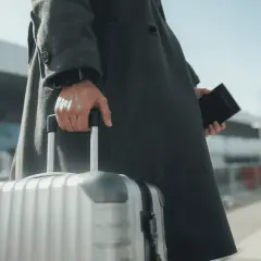 Osoba w płaszczu trzyma walizkę i paszport, gotowa do podróży. W kieszeni czeka karta EKUZ.