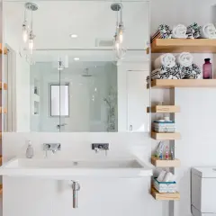 Salle de bain petite surface : lavabo double, étagères en bois flotté, miroir, douche vitrée et toilettes. Idée déco fonctionnelle.