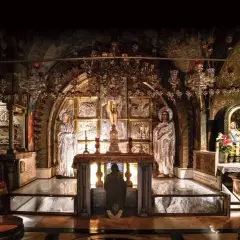 Wnętrze kaplicy na Golgocie, z ołtarzem, figurami i ikonami, gdzie wierni klęczą w zadumie.