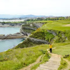 Persona con los brazos en alto en un acantilado verde, contemplando el mar y la costa. ¡Ideas para que ver en Cantabria en 4 días!
