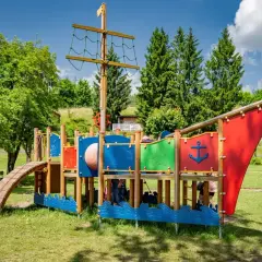 Kolorowy plac zabaw w kształcie statku pirackiego, z drabinkami i zjeżdżalnią, to wspaniałe atrakcje dla dzieci nad brzegiem jeziora.
