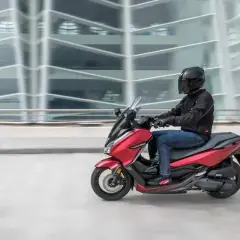 Czerwony skuter z kierowcą w kasku pędzi obok nowoczesnego budynku. To jak tuning 125 na 250, czysta moc!