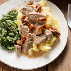 Polędwiczki z suszonymi pomidorami na kremowym purée, obok porcja szpinaku. Pyszny obiad gotowy do podania.