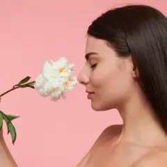 Kobieta wącha białą piwonię, szukając inspiracji, jak dobrać perfumy.