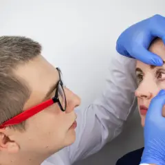 Lekarz w niebieskich rękawiczkach bada oko pacjentki, podejrzewając zapalenie rogówki.
