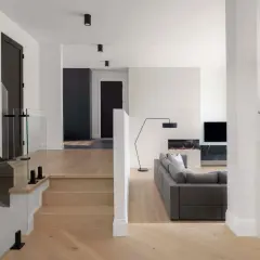 Modern split level home interior with a glass-railed staircase, a gray sectional sofa, and a fireplace.