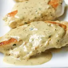 Deux morceaux de poulet à la crème, nappés d'une sauce onctueuse aux herbes, sur une assiette blanche.