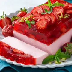 Pyszny sernik na zimno z galaretką i truskawkami, udekorowany miętą i pistacjami. Idealny na letnie popołudnie.