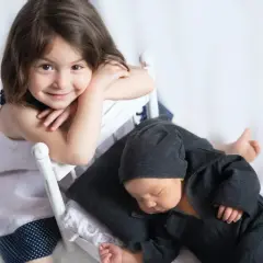 Niña sonríe mientras su hermanito duerme. Quizás ya no habrá rabietas por la llegada de un hermano.
