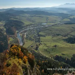 Widok z góry na dolinę Dunajca, miasteczko i góry w oddali, przypominające trzy korony. Jesienne barwy drzew na zboczu.