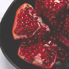 Ein aufgeschnittener Granatapfel in einer schwarzen Schale, voller saftiger Kerne. Ein Symbol für einen gesunden Lebensstil.