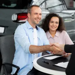 Un couple heureux finalise un accord de rachat de franchise avec un concessionnaire automobile, scellant leur nouvelle acquisition par une poignée de main.