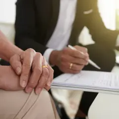 Para, która podpisuje intercyzę po ślubie, z dłonią na dokumentach. Mężczyzna w garniturze pisze piórem.
