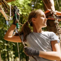 Ein Mädchen mit Zopf genießt den Ausblick im Kletterpark Wuppertal, während sie sich an einem Seil festhält.