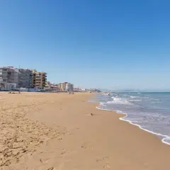Arena dorada y edificios vacacionales en la playa Roqueta, con el mar Mediterráneo azul y olas suaves.