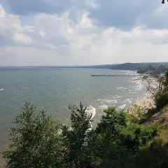 Widok na morze i plażę z klifu orłowskiego. W oddali widać molo i ludzi odpoczywających na piasku.