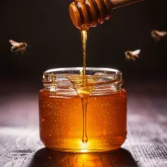 Un tarro de miel dorada, con abejas revoloteando, parece un sueño con miel.