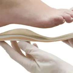 Fuß mit Plattfuß wird mit einer Einlage behandelt. Hände in Handschuhen halten die orthopädische Einlage.