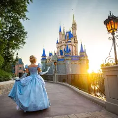 Kopciuszek w błękitnej sukni idzie w stronę zamku w Disneylandzie na Florydzie, podczas zachodu słońca.