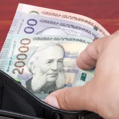 Dłoń wyciąga z portfela banknot 20000 dramów, waluta Armenii. Widoczne też inne banknoty.