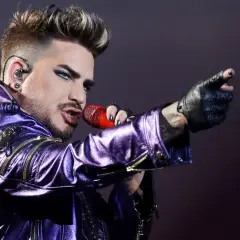 Adam Lambert w błyszczącej, fioletowej kurtce śpiewa z mikrofonem, wskazując palcem. To jakby Queen powrócił na scenę z nową energią.