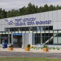 Nowoczesny budynek lotniska w Zielonej Górze-Babimoście z dużymi oknami i napisem "PORT LOTNICZY ZIELONA GÓRA-BABIMOST".