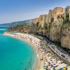 Tropea lotnisko: malownicza plaża z turkusową wodą, kolorowe budynki na klifie i droga z samochodami.