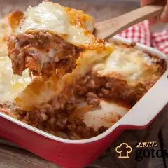 Gorąca, pachnąca lasagne z mięsem i serem, właśnie nakładana drewnianą łopatką. Idealna na rodzinny obiad.