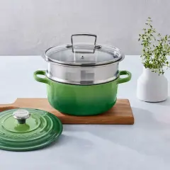 Grön kastrull med ånginsats, redo att ånga mat. Bredvid en skärbräda, en grön lock och en liten skål med mandlar.