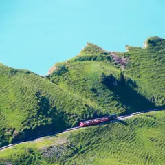 Rött tåg med passagerare på en bergssluttning vid en turkos sjö, en dröm för alla som älskar tåg interrail.