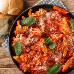 Pyszne flaki po rzymsku w sosie pomidorowym, posypane parmezanem i udekorowane miętą. Obok świeże pieczywo.