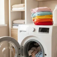 Stos kolorowych pieluch tetrowych na pralce z otwartymi drzwiczkami.