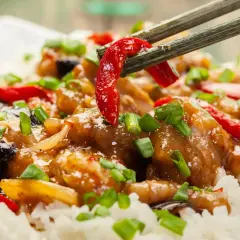 Schab po chińsku z ryżem, posypany szczypiorkiem. Pałeczki podnoszą kawałek papryczki chili z aromatycznego dania.