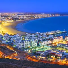 Agadir, Marocko, upplyst vid skymningen. En livlig stad vid havet med en strandpromenad, en marina och ljusspår från trafiken.