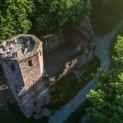 Blick von oben auf die Ruine der Barbara Kapelle, umgeben von grünen Bäumen. Eine Gruppe von Menschen genießt die Aussicht vom Turm.