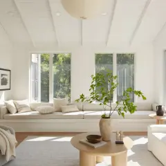 A bright living room with neutral interior design, featuring a large window seat, a textured armchair, and a light wood coffee table.