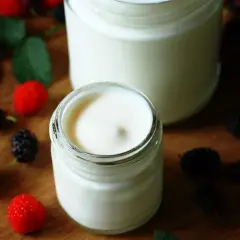 Dos frascos de yogurt casero cremoso, decorados con moras y hojas verdes. Una guía visual para aprender como hacer yogurt casero.