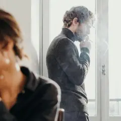 Coppia in crisi, lui fuma vicino alla finestra, lei distratta. Un parere psicologo sulla coppia aperta potrebbe aiutare.
