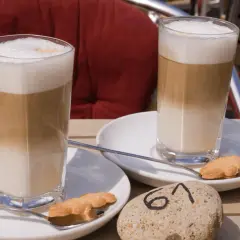 Dwa latte macchiato z pianką i ciasteczkiem na talerzyku, obok kamień z numerem 61.