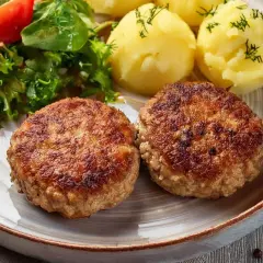 Dwa apetyczne kotlety mielone z airfryer, podane z ziemniakami i świeżą sałatką.